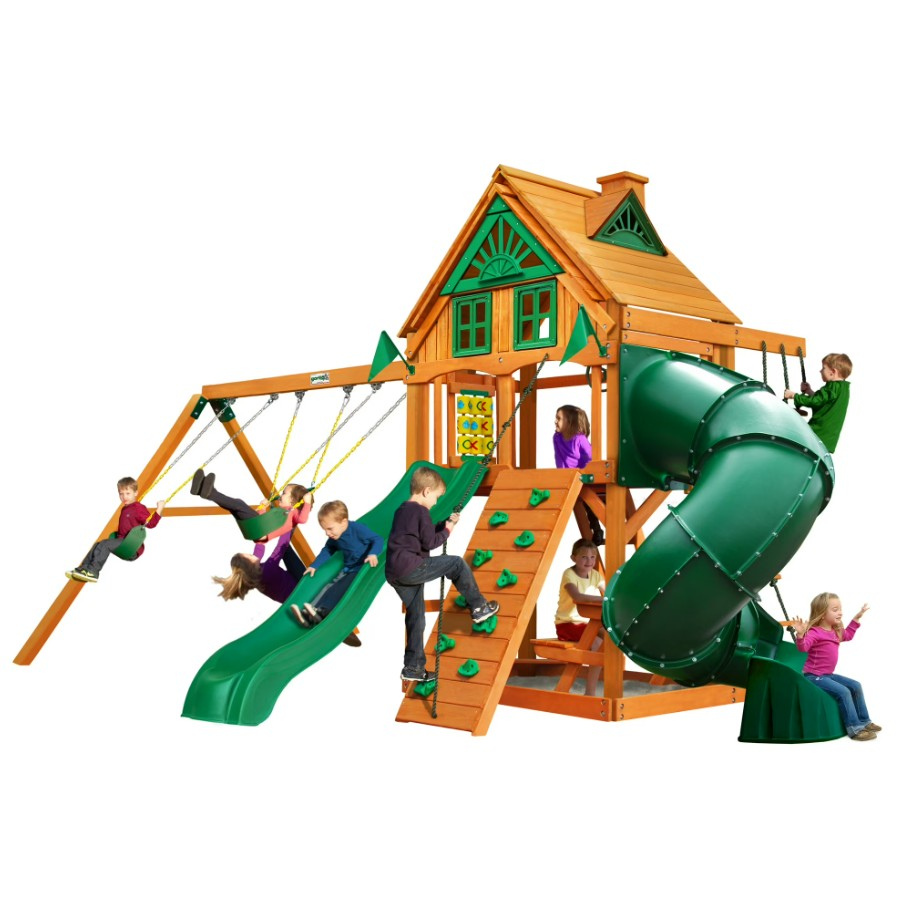 Children play on the Gorilla Playsets Mountaineer Treehouse Wooden Swing Set, which features swings, a tube slide, a rope ladder, and a sandbox.