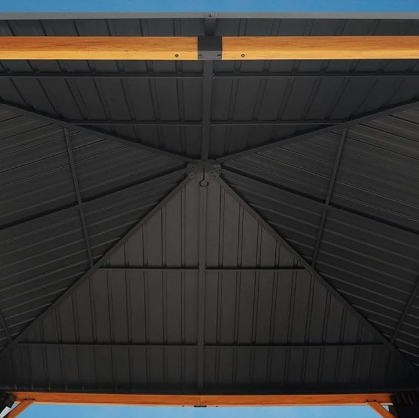Enjoy the view from beneath the 10 ft x 10 ft Wood Grain Outdoor Patio Gazebo with Metal Roof, featuring a geometric-patterned hardtop canopy supported by elegant wooden-style beams, set against a clear blue sky.